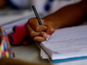 Mão de criança negra escrevendo com lápis em um caderno